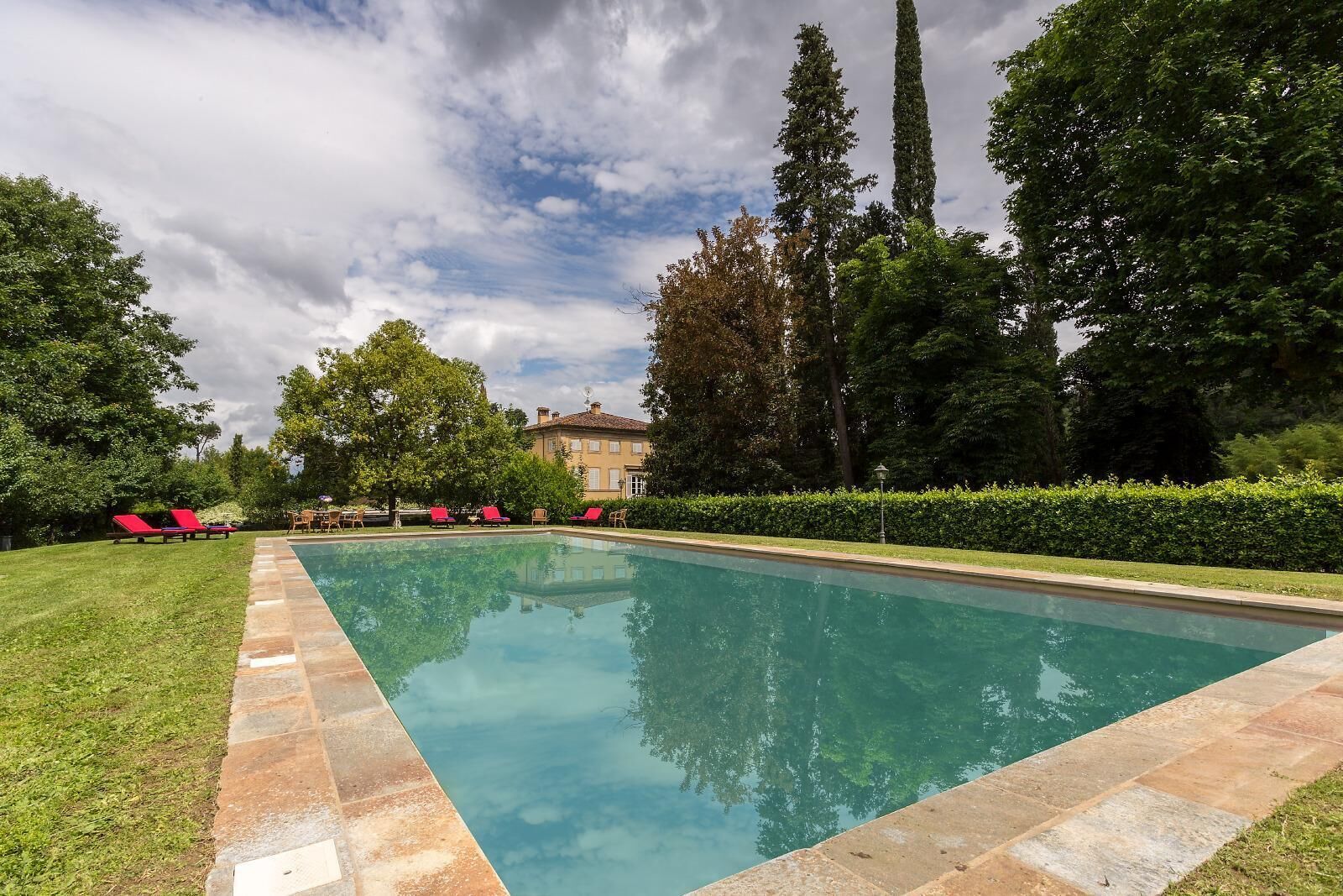 Une piscine rectangulaire bordée de carreaux, entourée d’une pelouse bien entretenue et de chaises longues rouges.