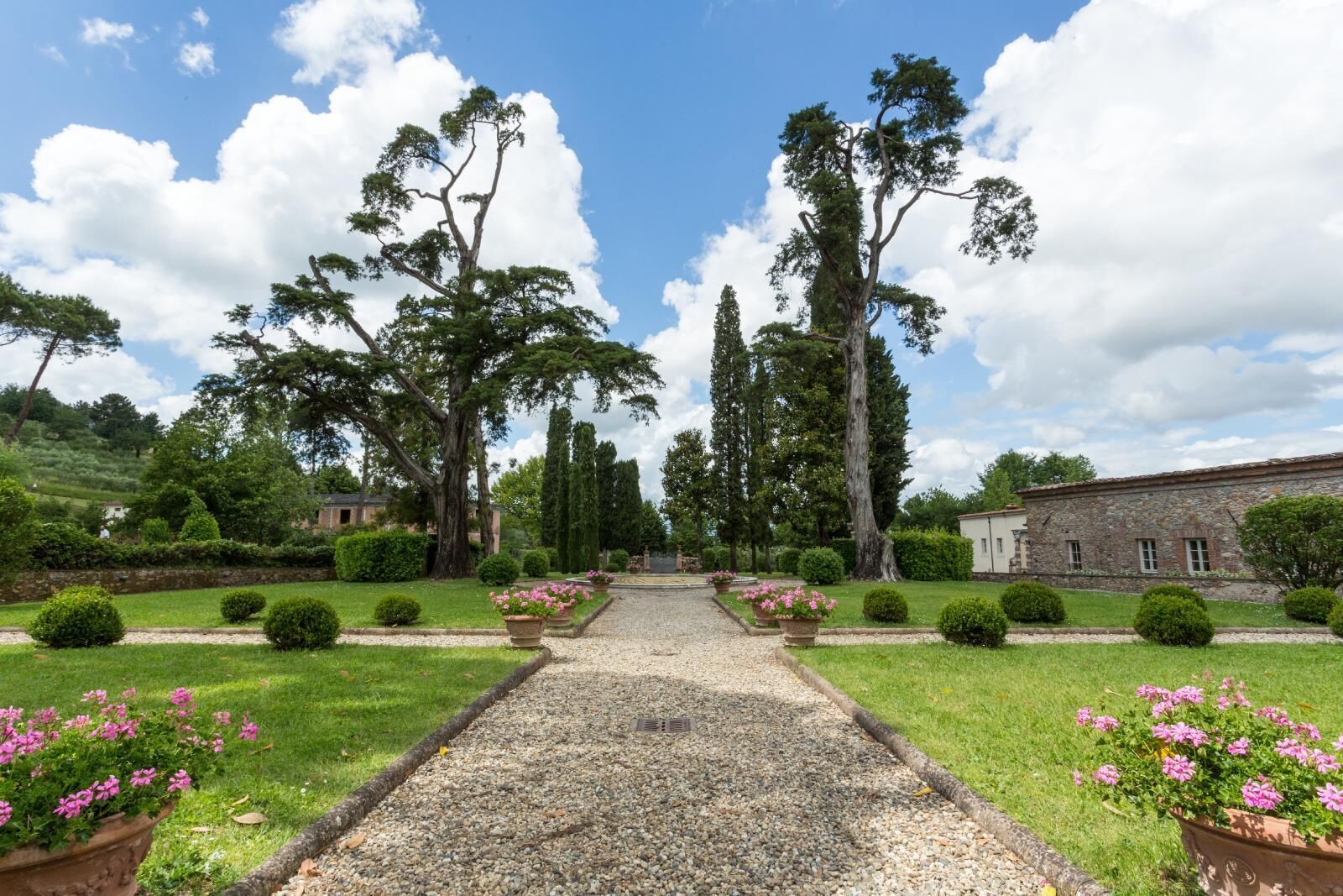 A garden pathway leading to a building with a stone facade, surrounded by well-maintained hedges and flowering plants.