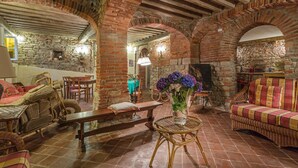 Un intérieur rustique avec des arches en briques, des meubles en osier et une table centrale agrémentée d’un vase de fleurs.