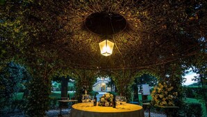 Un espace de restauration en plein air avec une table dressée pour deux personnes, entouré d’une végétation luxuriante et surmonté d’une lanterne décorative.