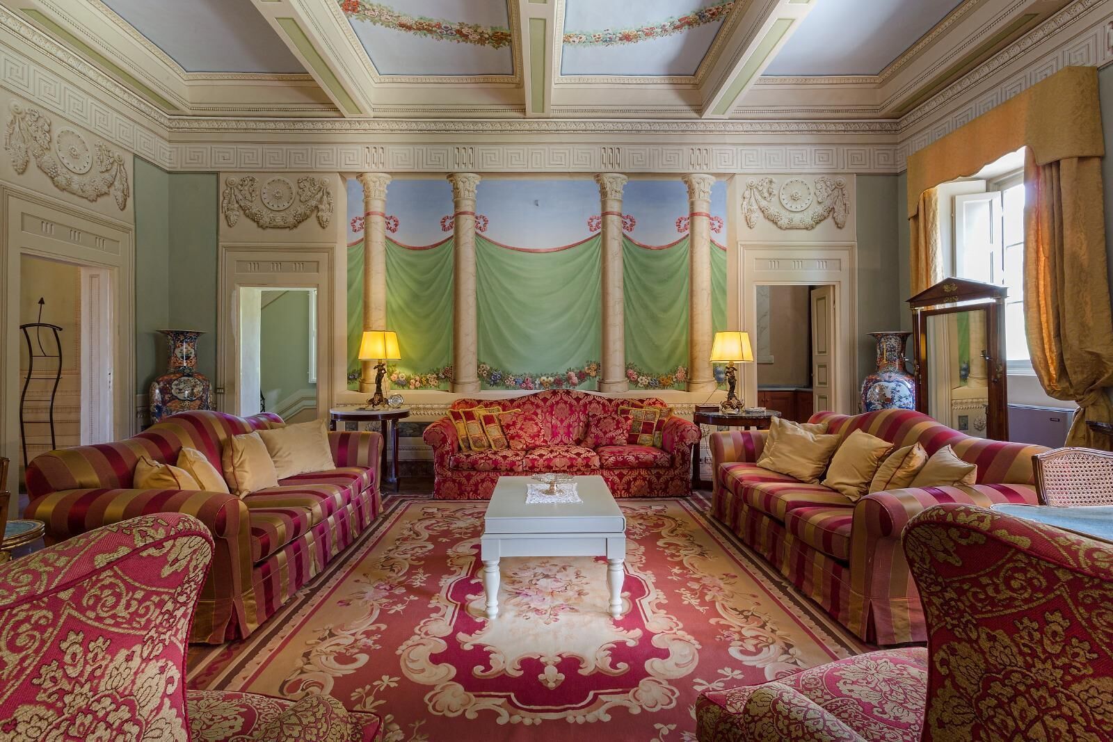 A luxurious room with a central red sofa, two armchairs, a coffee table, and a patterned carpet.