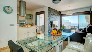 Une cuisine moderne avec un coin repas comprenant une table et des chaises en verre, un mur décoratif en pierre et une vue sur l’océan.