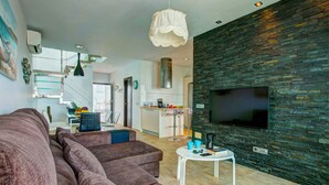 Un salon moderne avec un grand canapé, une table basse blanche et un téléviseur à écran plat fixé sur un mur à texture.