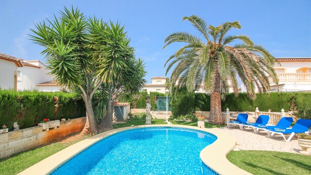 A swimming pool with blue tiles, surrounded by palm trees and a white building with a tiled roof. - Villa with pool in Denia La Giralda BO (Denia)