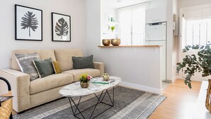 A living room with a beige sofa, a round coffee table, and two framed leaf artworks. - Genteel Home Trinidad Grund C (Málaga)