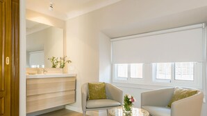 A modern living room with a sofa, a coffee table, and a large window with blinds. - Genteel Home Trinidad Grund C (Málaga)