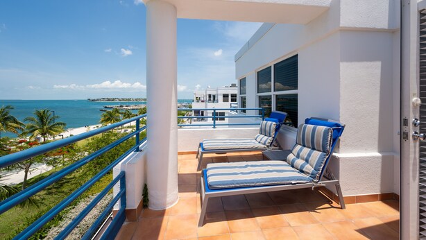 Een balkon met twee lounge fauteuils, uitzicht op de oceaan en een wit gebouw op de achtergrond.