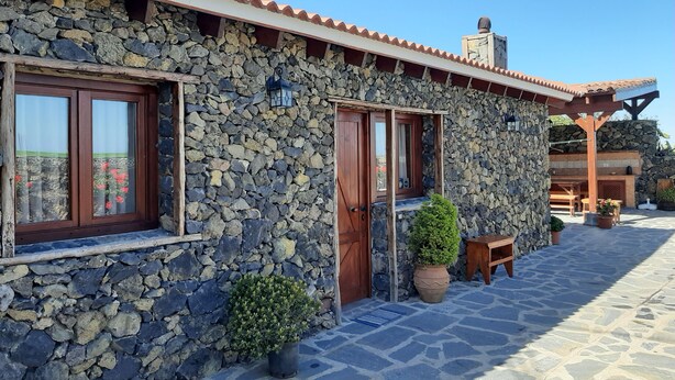 A stone building with a tiled roof, wooden doors, and windows with curtains.