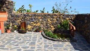 A stone patio with potted plants, a small pond, and a wooden structure.