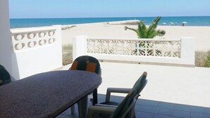 Een terras met een tafel en stoelen, uitkijkend op een strand met een helder uitzicht op de oceaan.
