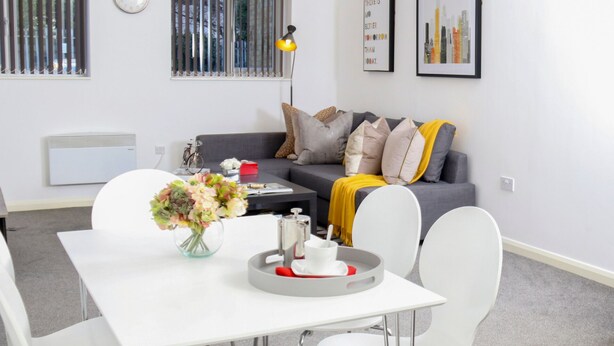 A modern living room with a grey sofa, white chairs, a dining table, and a vase of flowers.