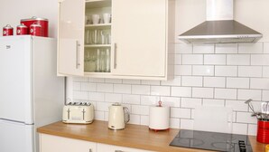 A kitchen with a white refrigerator, a cabinet with glass doors, a toaster, a kettle, a roll of paper towels, and a red utensil holder.