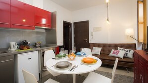 Een compact woongedeelte met een kitchenette, een eethoek en een bank met kussens.