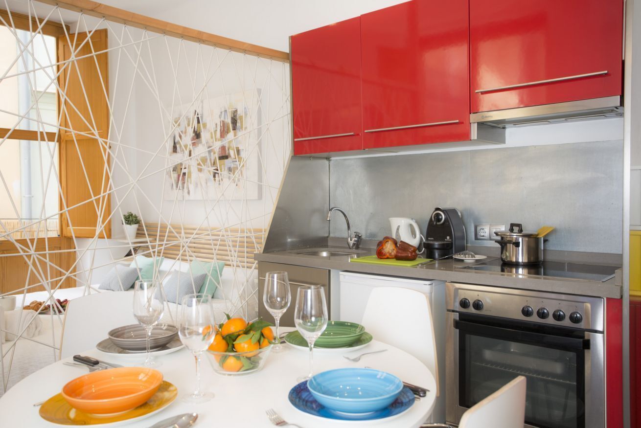 A modern kitchen with red cabinets, stainless steel appliances, and a dining area with a white table set with plates and glasses.