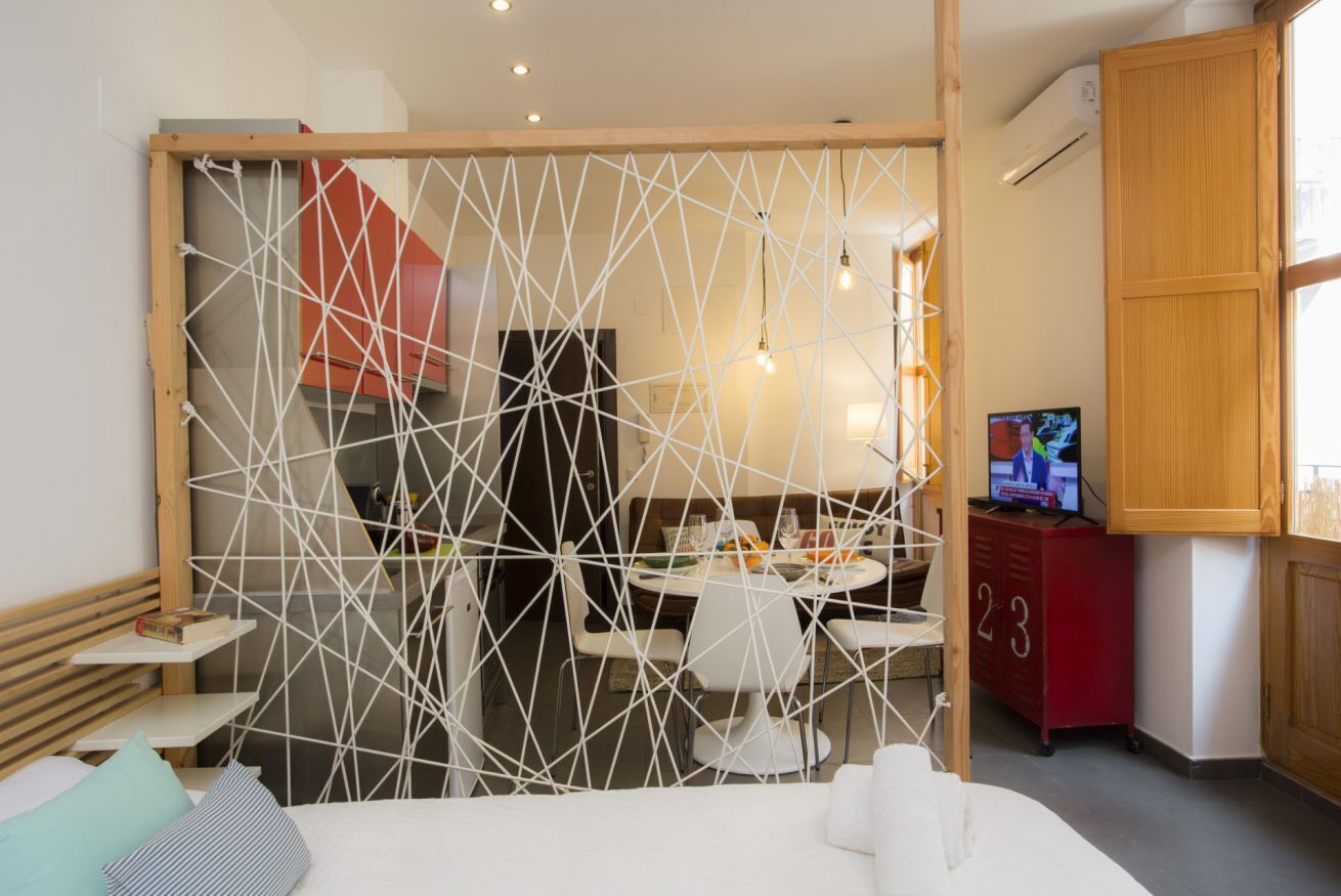 A modern hotel room with a bed, a dining area, and a TV.