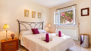Un dormitorio con cama, lámparas de noche, una ventana con vistas a flores rosadas y un radiador.