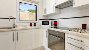Una cocina moderna con armarios blancos, un lavamanos de acero inoxidable, un microondas y un lavavajillas.