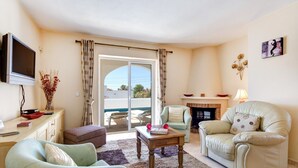 Una sala de estar con un sofá, un sillón y una mesa de centro. Hay una chimenea, un televisor y una ventana con cortinas.