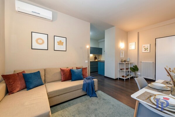 A living room with a sofa, a dining table set for two, and a kitchen in the background.