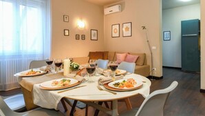 A dining area with a round table set for four, surrounded by grey chairs. There are two framed pictures on the wall, a floor lamp, and a refrigerator in the background. - Desenzanoloft A Casa di Sara  (Desenzano del Garda)