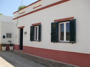 A building with two windows, a door, and a small sign on the wall. - Casa Magaída, AC, with terrace, near the Ria (Luz (Luz de Tavira))