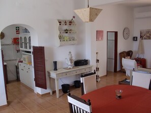 Un coin repas avec une table rouge, des chaises blanches, un meuble blanc avec des étagères, une horloge et une lampe.