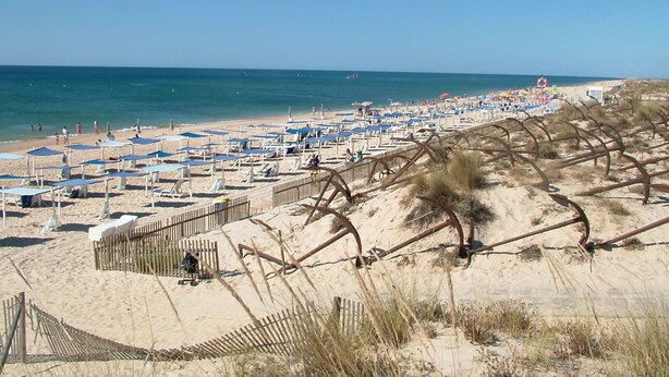 A beach with rows of sun loungers and umbrellas, a sandy area with a wooden fence, and the ocean in the background. - Casa Magaída, AC, with terrace, near the Ria (Luz (Luz de Tavira))