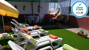 A sunlit outdoor seating area with white lounge chairs, some with orange and green cushions, and a yellow umbrella providing shade. - Casa Magaída, AC, with terrace, near the Ria (Luz (Luz de Tavira))