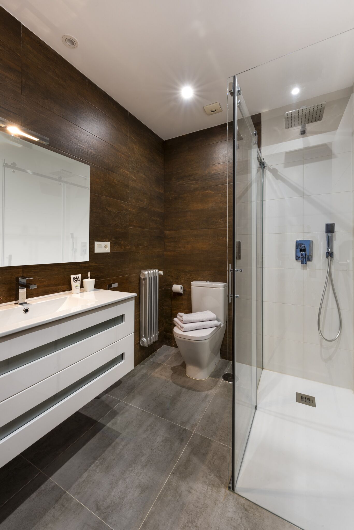 Un baño moderno con cabina de ducha de vidrio, un lavabo blanco con espejo y un inodoro con toalla.