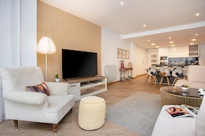 A modern living room with a flat-screen TV, a sofa, a coffee table, and a dining area with chairs and a small table. - Genteel Home Tablas - Four Bedroom Apartment, Sleeps 8 (Granada)