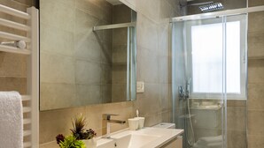 Un baño moderno con un espejo grande, un tocador blanco, una cabina de ducha de vidrio y un inodoro blanco.
