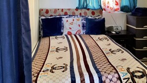 A bedroom with a bed, a window with curtains, a radiator, and a small table with a radio. - Higuey Center City, George City (Higuey)
