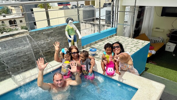 A rooftop pool with a view of buildings, a railing, and a baby pool. - Higuey Center City, George City (Higuey)