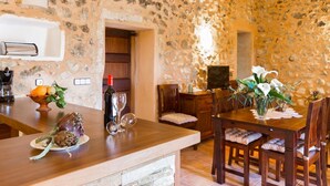 A rustic stone interior with a wooden dining table, chairs, and a wine bottle.