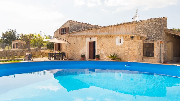 A stone building with a swimming pool, outdoor furniture, and potted plants.