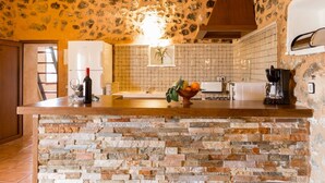 A kitchen with a stone wall backsplash, a wooden island, and a hanging light fixture.