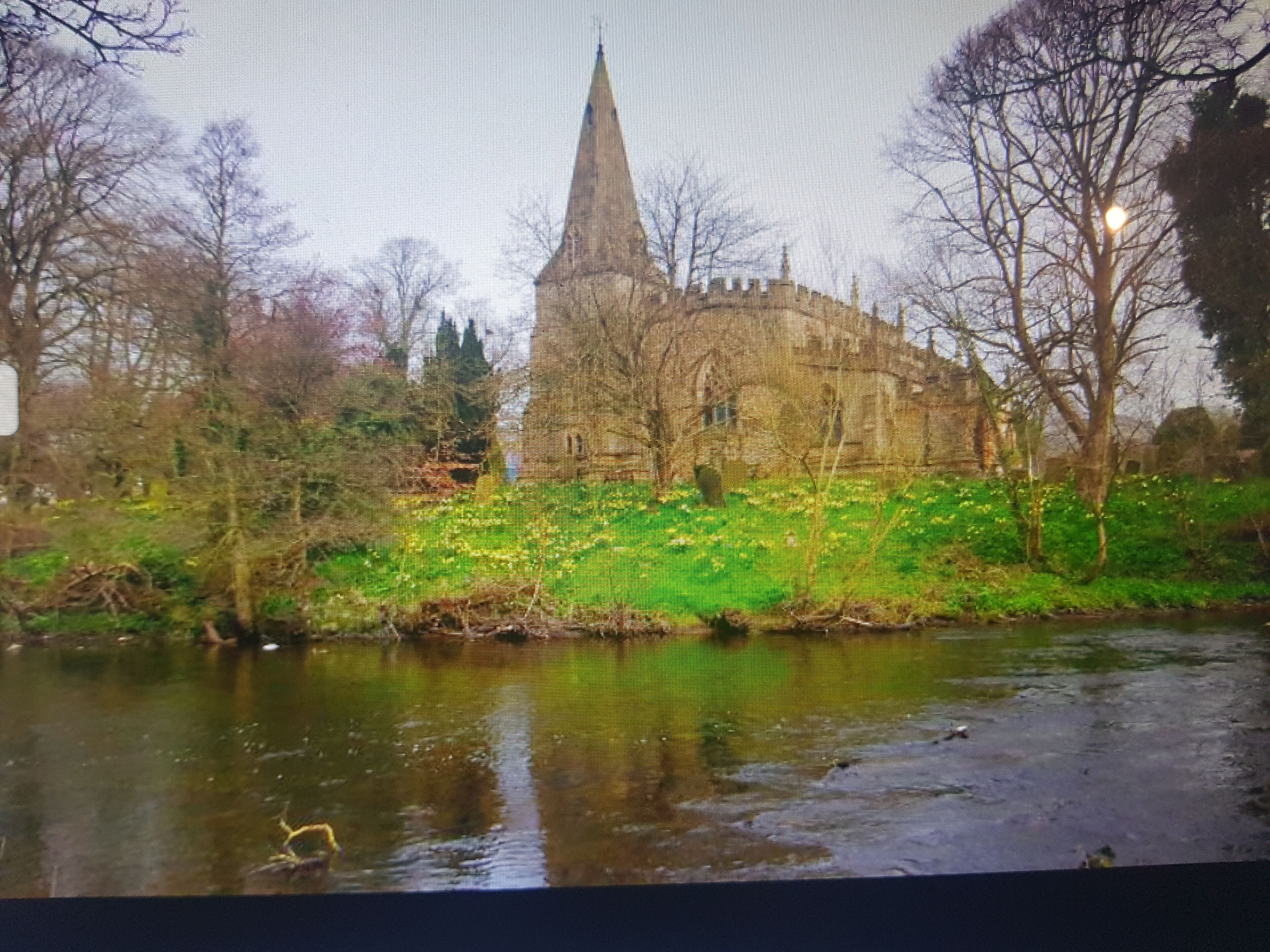A historic building with a prominent tower, surrounded by trees and a body of water.
