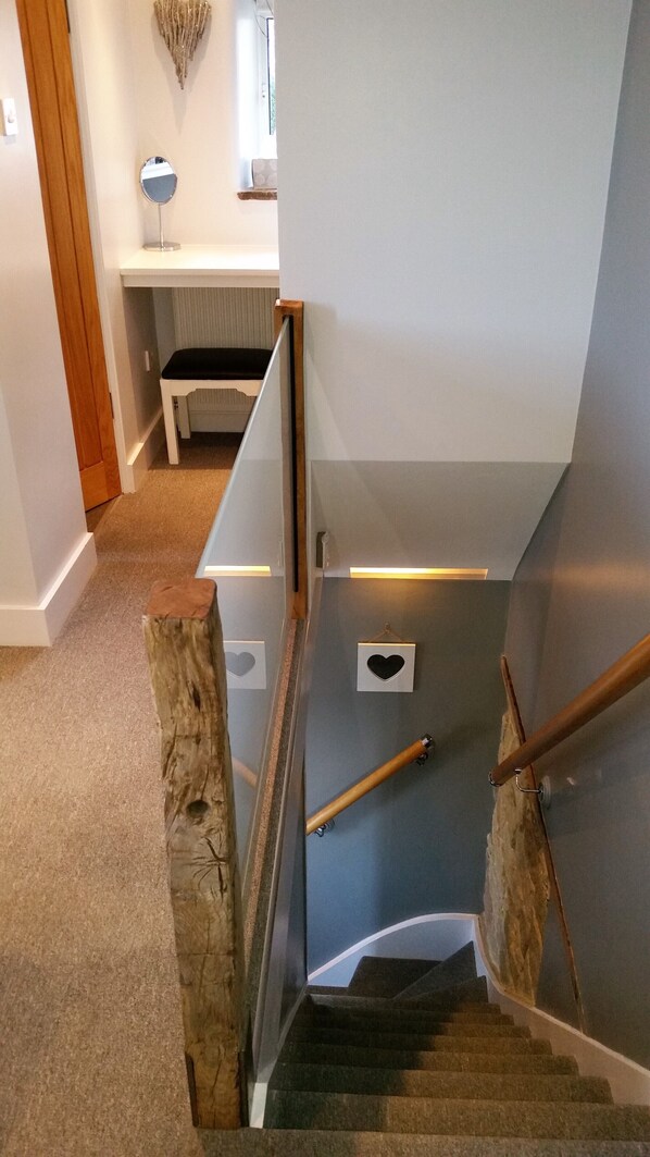 Una escalera con barandilla de madera, una mesita con espejo y una decoración en forma de corazón en la pared.