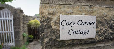 Een stenen muur met een bord waarop 'Cosy Corner Cottage' staat.