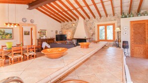 A spacious living area with a high ceiling, stone walls, and wooden beams. There is a fireplace, a television, and various decorative items.