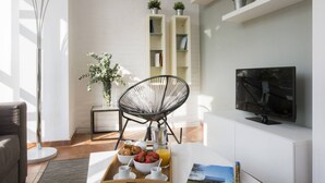 A modern living room with a white sofa, a black chair, a coffee table with breakfast items, a TV, and a bookshelf with plants. - Singular Stays Botanico 201 (València)