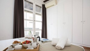 A hotel room with a bed, a breakfast tray with pastries, a coffee pot, and a window with curtains. - Singular Stays Botanico 201 (València)
