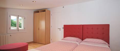 Ein Schlafzimmer mit einem Bett, einem roten Pouf, einem Kleiderschrank und einem Fenster.