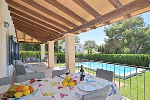 An outdoor patio with a table set for two, a pool, and a view of the surrounding garden. - Camamila - Modern house with pool in Bonaire, Alcúdia (Alcúdia)