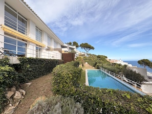 A modern building with a swimming pool, surrounded by lush greenery and a clear view of the sea. - Holiday rental semidetached with swimming pool in Begur, Sa Tuna (Begur)
