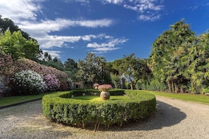 A landscaped garden with a circular hedge, a central planter, and a gravel path. - Villa Controni     . (Capannori)
