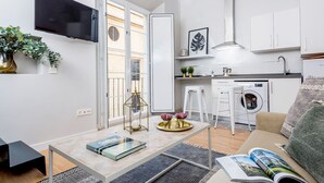 A modern apartment with a kitchen, dining area, and living room. It includes a flat-screen TV, a washing machine, and a dining table with chairs.