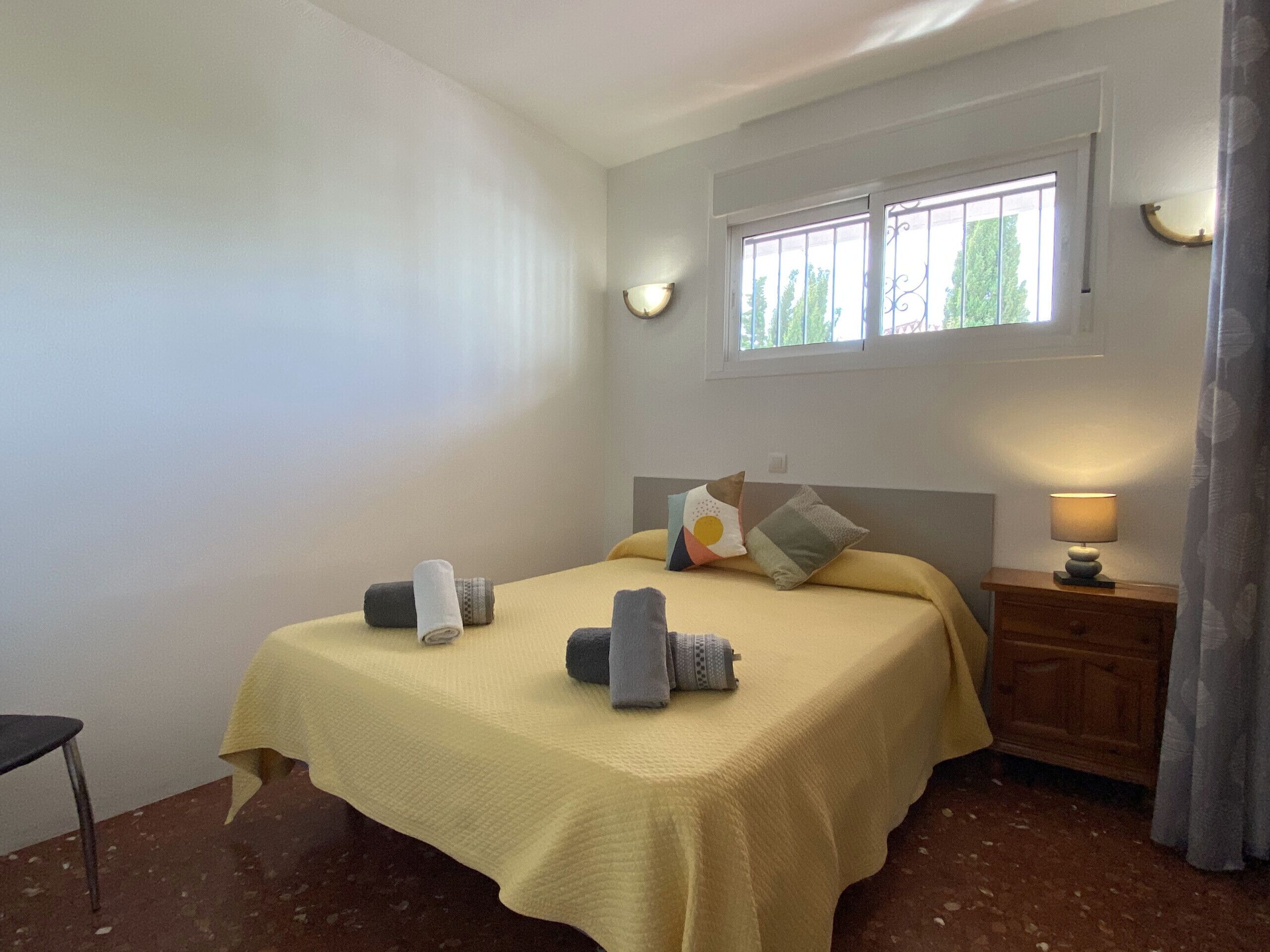 Een slaapkamer met een bed, nachtkastje, lamp en raam.