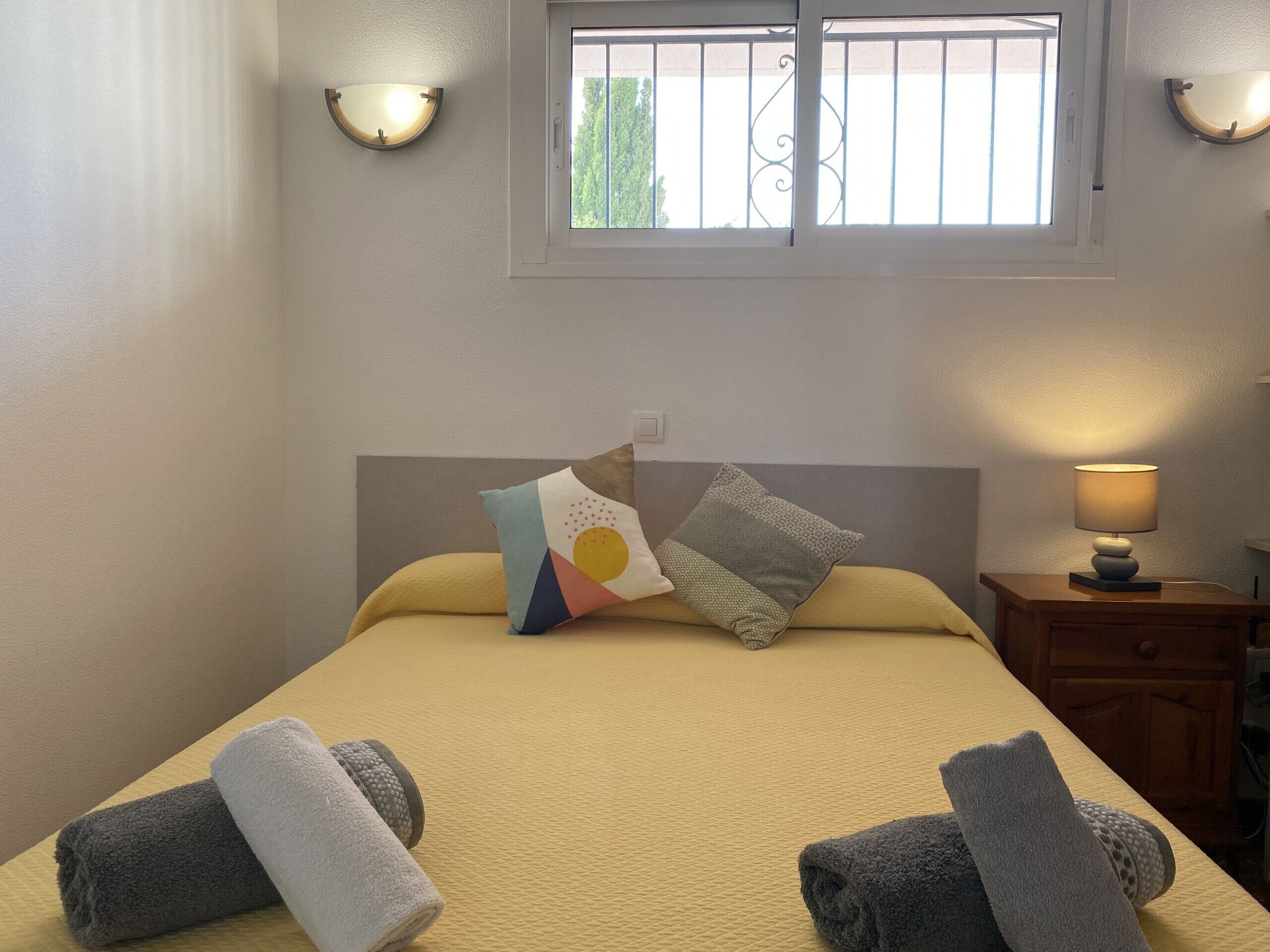 Een net opgemaakt bed met twee handdoeken, een bedlampje en twee wandlampen.