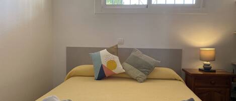 Een net opgemaakt bed met twee handdoeken, een bedlampje en twee wandlampen.